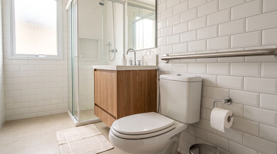Banheiro com barra de apoio de inox instalada ao lado do vaso sanitário